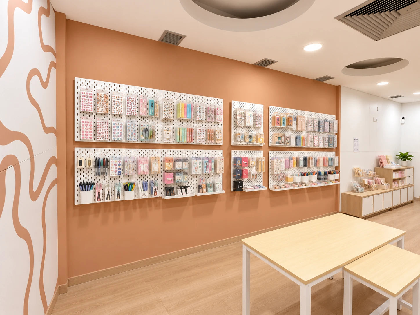 El interior de ARU PAPER: una pared de color teja con paneles blancos llenos de pegatinas, rotuladores y washi tape, y una mesa de madera clara delante